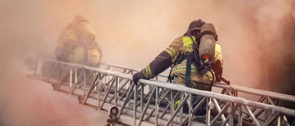 vigili del fuoco si arrampicano su una scala all'interno di una casa in fiamme, attraversando il fumo