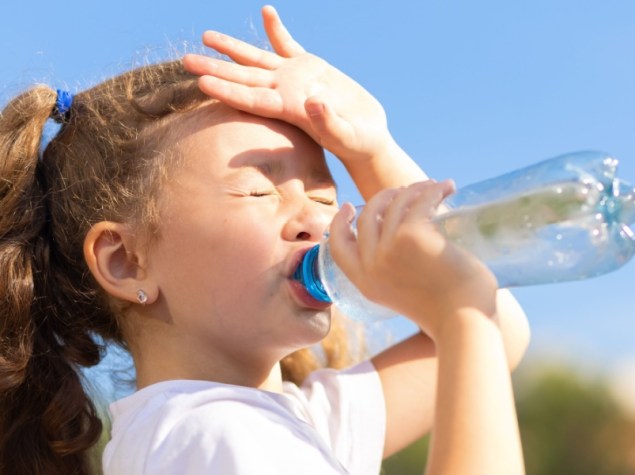 Bambina che beve acqua da una bottiglia con il caldo
