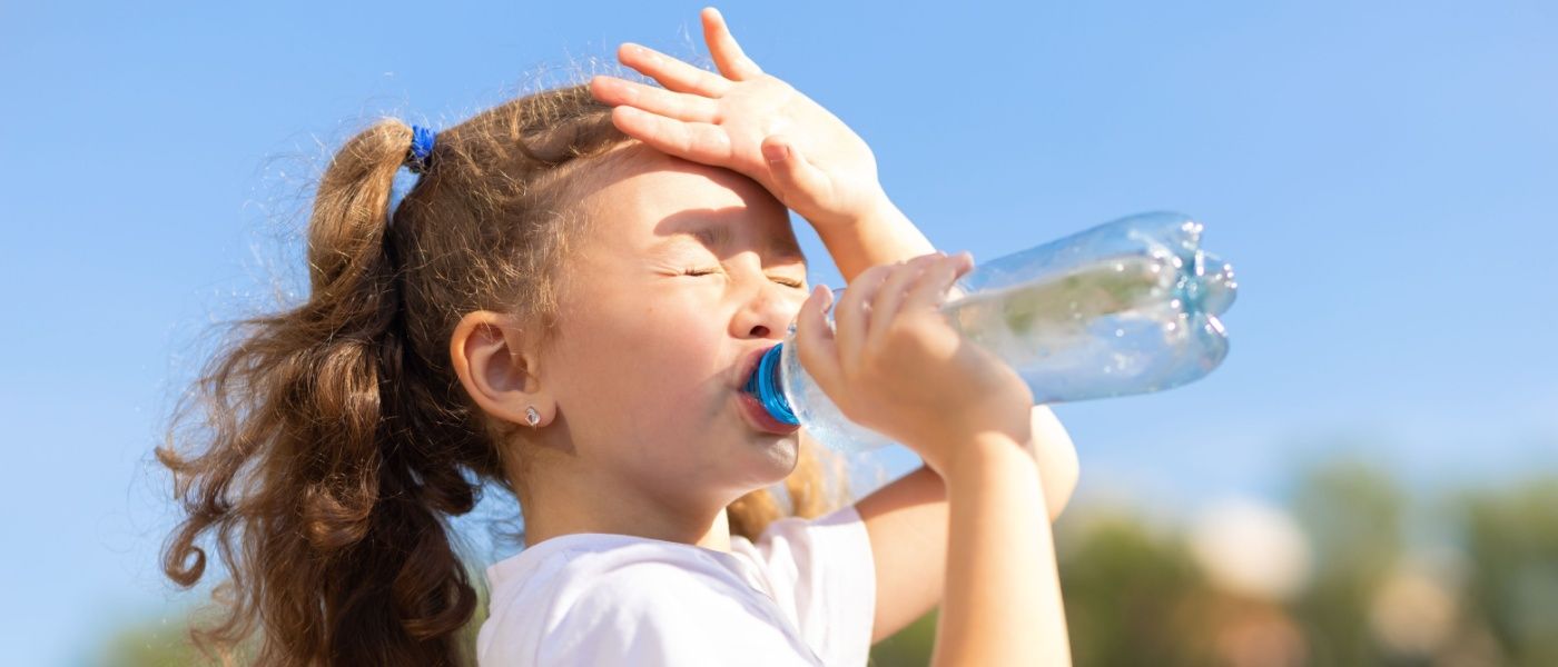 Bambina che beve acqua da una bottiglia con il caldo