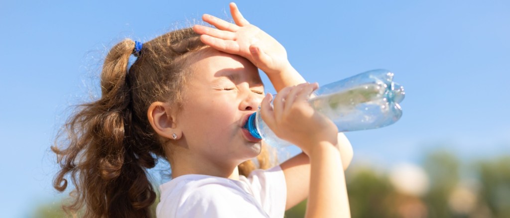 Bambina che beve acqua da una bottiglia con il caldo