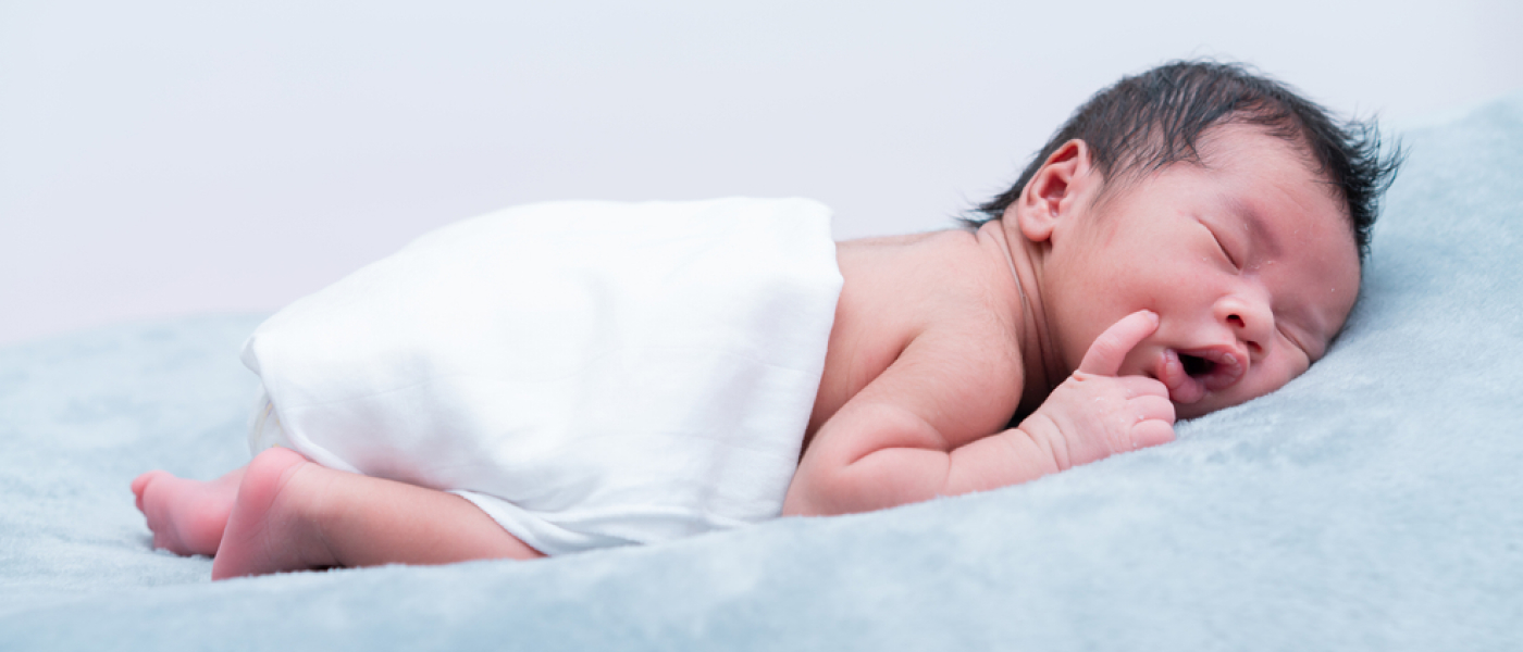 Baby boy lying prone on grey bed, side view
