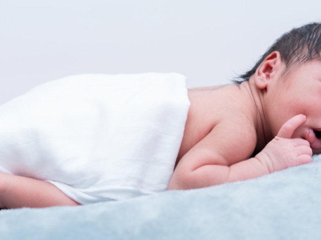 Baby boy lying prone on grey bed, side view