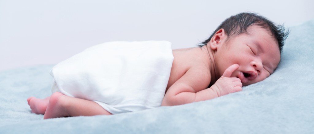 Baby boy lying prone on grey bed, side view