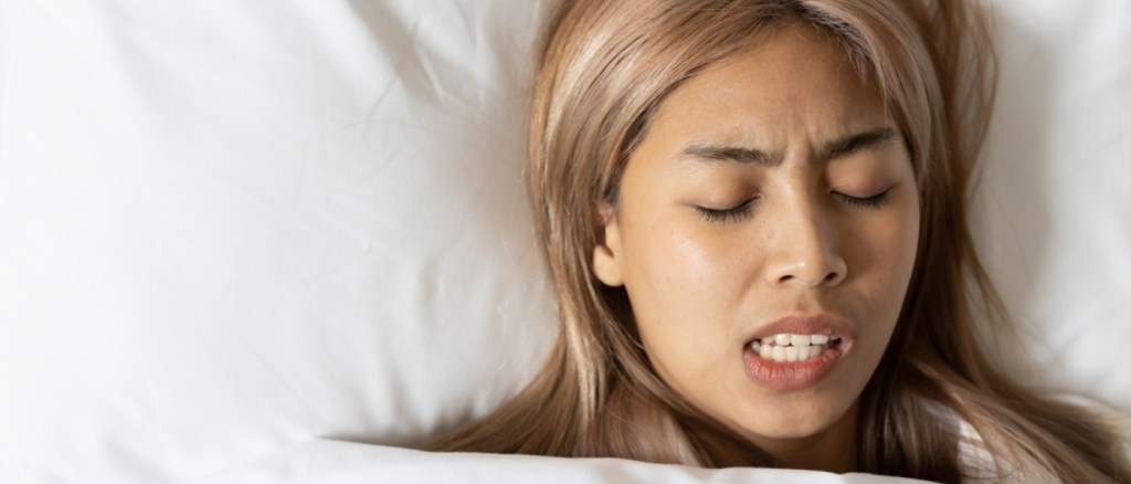 Tired and stressed Asian woman with colored hair sleeping, having bad dream, nightmare with bruxism or grinding teeth
