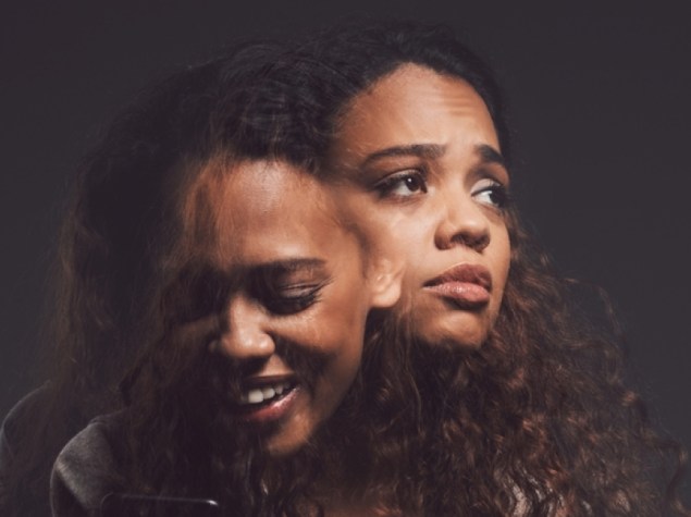 Depression, mental health and woman in studio with stress, identity crisis or bipolar disorder. Horror, psycho and female person with trauma or anxiety browsing on a phone by a dark black background.