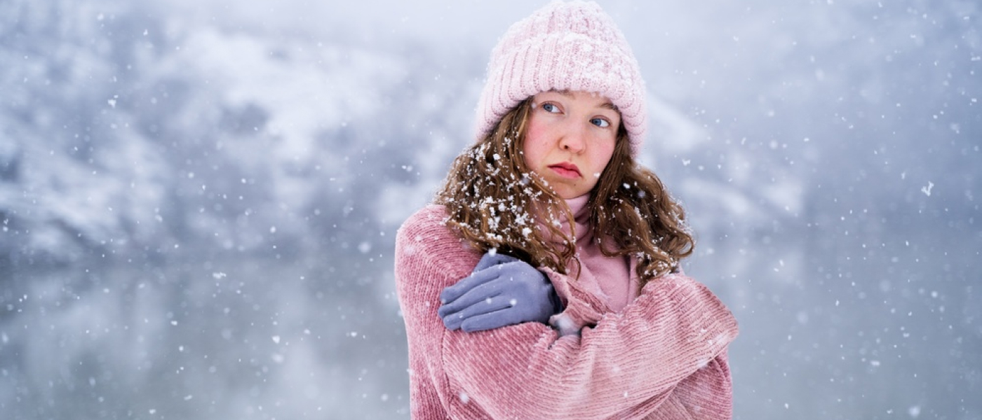 Ritratto di giovane donna fredda che cerca di mantenere caldo all'aperto in inverno, sentendosi freddo in piedi vicino al lago in montagna alla luce del giorno, emozione del tempo freddo e concetto di disagio invernale