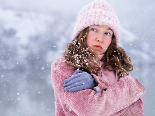 Ritratto di giovane donna fredda che cerca di mantenere caldo all'aperto in inverno, sentendosi freddo in piedi vicino al lago in montagna alla luce del giorno, emozione del tempo freddo e concetto di disagio invernale